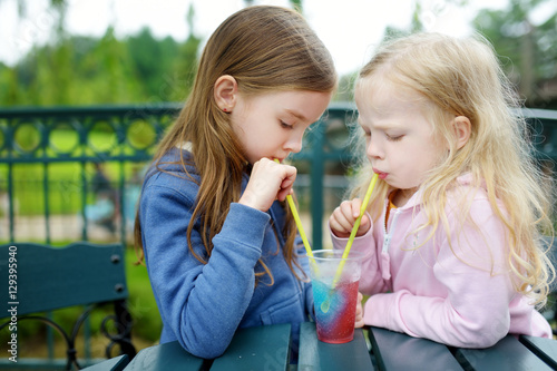 Foto Two cute little sisters drinking frozen slushie drink