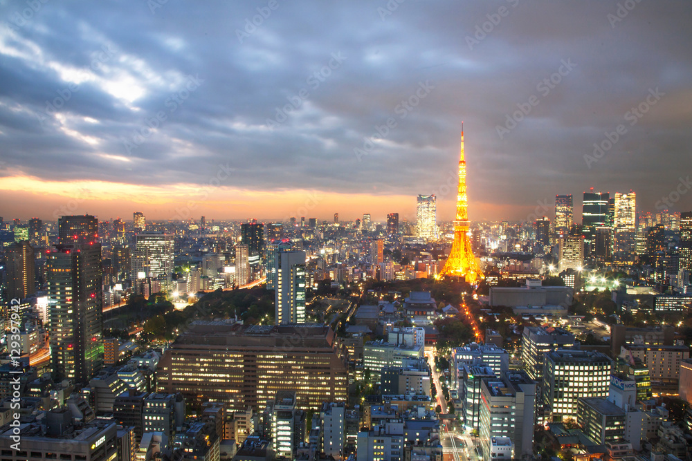 Fototapeta premium Oświetlony Tokyo Tower pośród pejzażu miejskiego z niebem o zachodzie słońca
