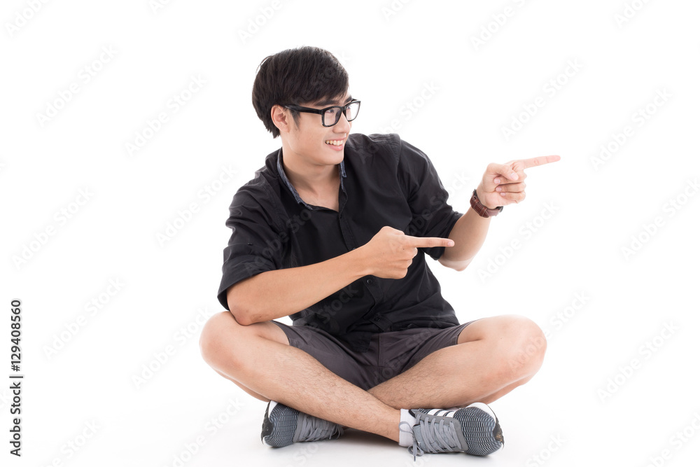 Young man sitting on the floor, pointing and looking to his side Young man sitting on the floor, pointing and looking to his side