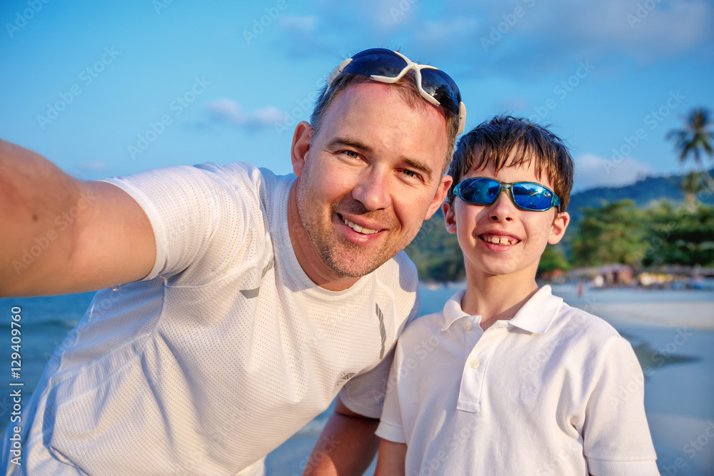 Cute little boy and his father making selfie at tropical beach on exotic island