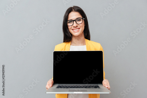 Pretty woman showing laptop display to camera over grey background photo