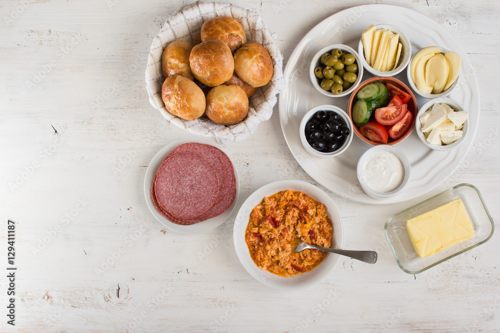 Traditional Turkish breakfast, top view: cooked egg menemen, pogaca pasties, vegetables, cheeses, olives and halal turkey salami, selective focus; copy space for text Traditional Turkish breakfast, top view: cooked egg menemen, pogaca pasties, vegetables, cheeses, olives and halal turkey salami, selective focus; copy space for text