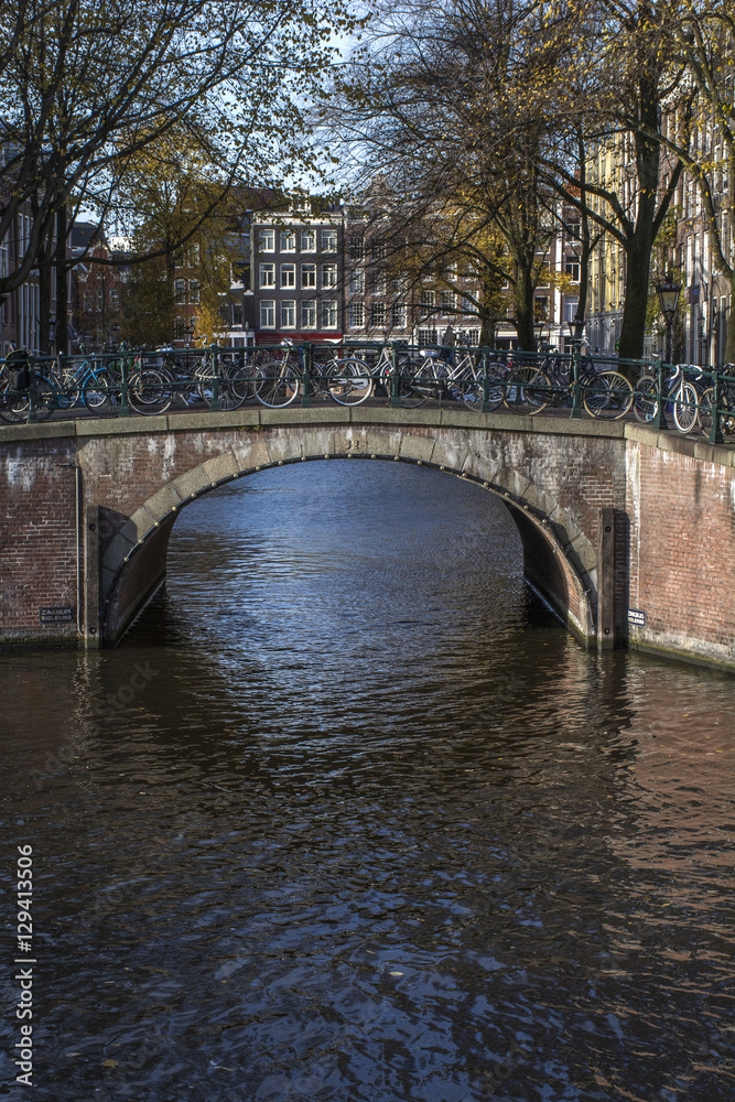 Old brown bridge with bikes over the canal in autumn in the day in Amsterdam