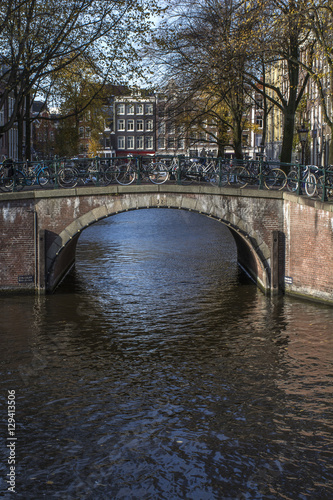 Old brown bridge with bikes over the canal in autumn in the day in Amsterdam