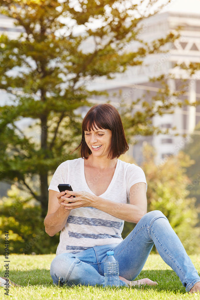 Happy woman sitting in grass with water with cellphone Happy woman sitting in grass with water with cellphone