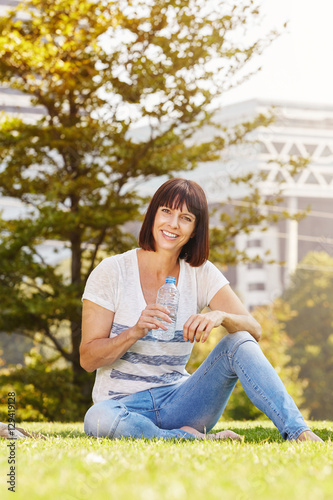 Smiling older woman with water bottle sitting in grass