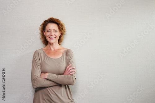 Older woman smiling with arms crossed by wall photo