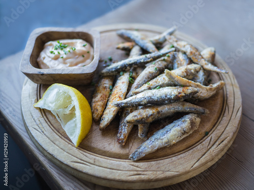 Canvas-taulu Whitebait, small fried fish served on a wooden rustic platter and wooden table with a dip and lemon
