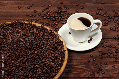 A cup of coffee on a wooden table. Coffee beans in a large dish.