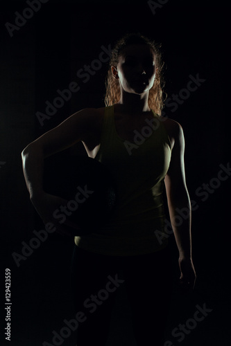 Young woman stands with the ball backlight and shadow in gym