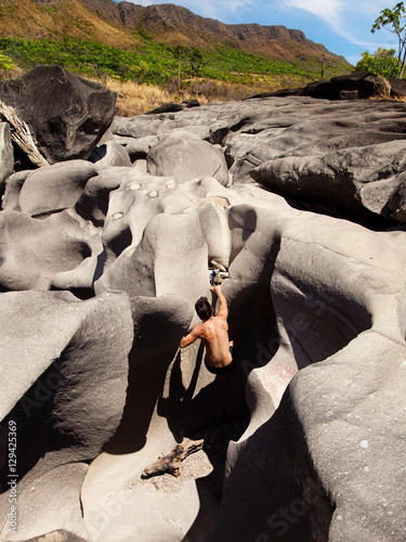 Young man climbs on boulders rocks in The Moon Valley, Chapada dos Veadeiros, Brazil