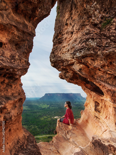 A woman admires the forest landscape sitting on a hole in a rock in Chapada das Mesas, Brazil
