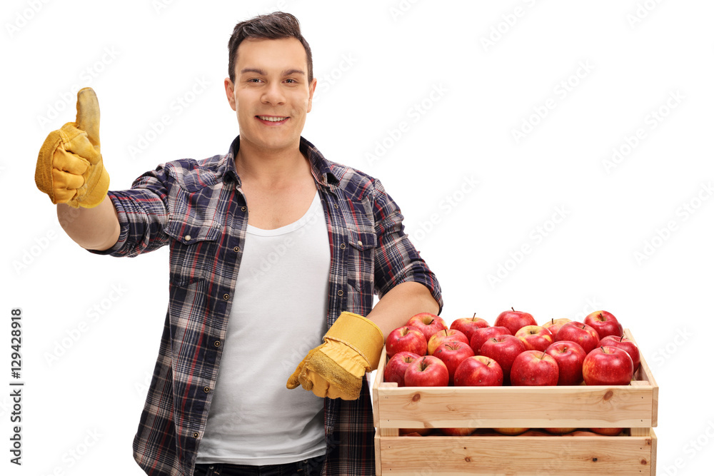 Joyful farmer leaning on a crate filled with apples and giving a Joyful farmer leaning on a crate filled with apples and giving a