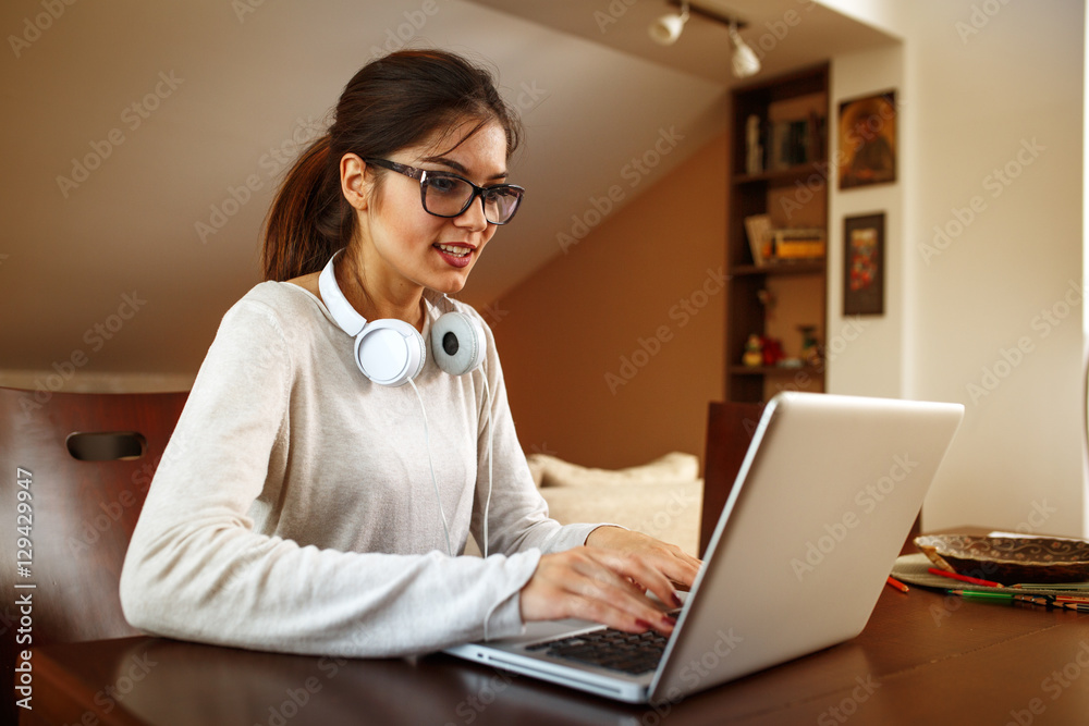 Young female student at home.She sitting in her living room and typing something on laptop.E-learning. Young female student at home.She sitting in her living room and typing something on laptop.E-learning.