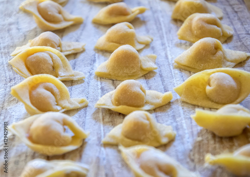  Raw italian cappelletti, fresh homemade pasta stuffed with cheese and meat on rustic wood table. Natural light.