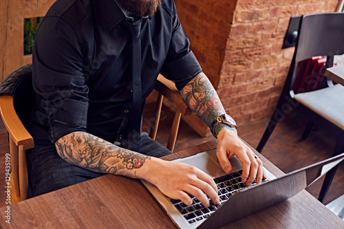 A man with tattooed arms working with a laptop.
