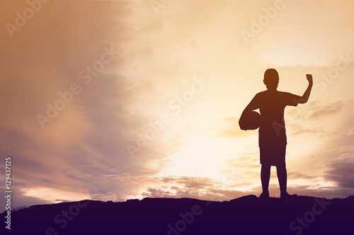 Fototapeta Naklejka Na Ścianę i Meble -  Silhouette little boy holding football on sun sky background.