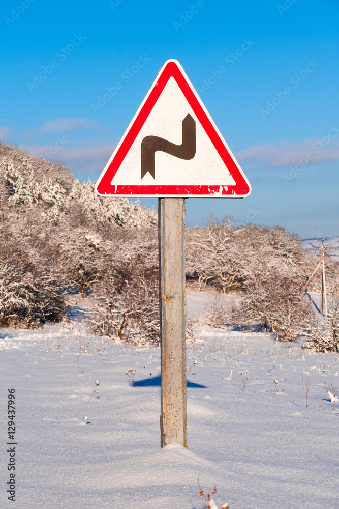 road sign concept steep turn / Road sign on snow-covered road in the countryside