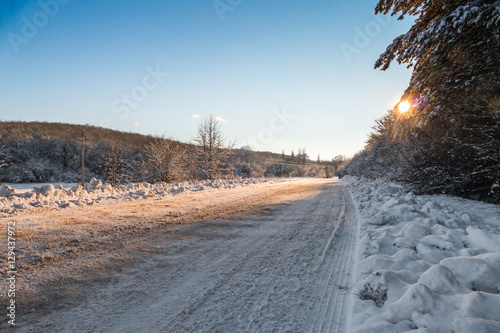 Snow-covered road in forest / Snow-covered road with anti-slip reagent in countryside in sunny day 
