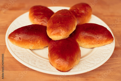 Oven fresh home made baked patties stuffed with eggs and green onionon on rustic wooden background. Home cuisine. Close up delicious stuffed home cooking pastries on a white plate. photo