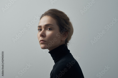 Dramatic portrait of a young beautiful girl with freckles in a black turtleneck on white background in studio © Parad St