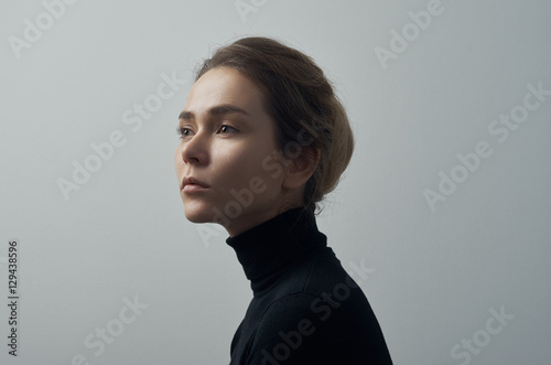 Dramatic portrait of a young beautiful girl with freckles in a black turtleneck on white background in studio photo