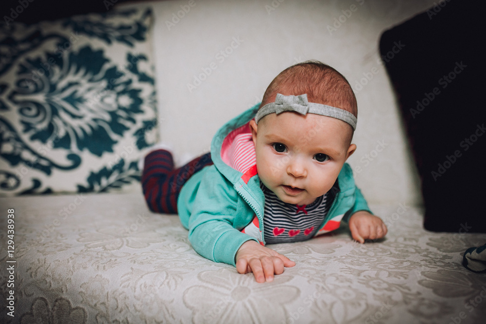 Fototapeta premium Baby girl plays on the couch at home. Baby newborn attentively looks.