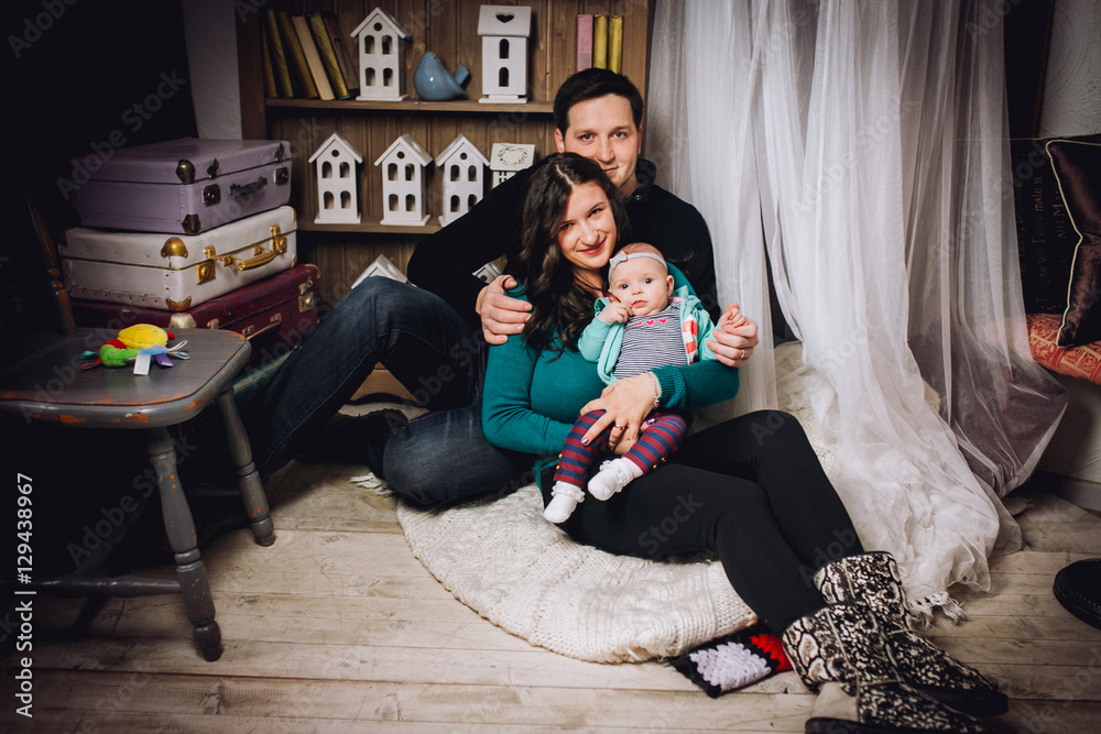 Happy parents with baby on the couch at home interior. Lifestyle, family and togetherness concept. Portrait a young playful family at home.