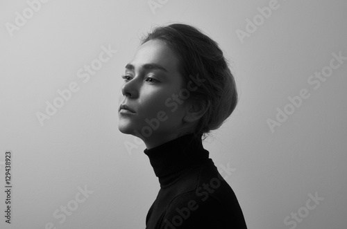 Dramatic black and white portrait of young beautiful girl with freckles in a black turtleneck on white background in studio