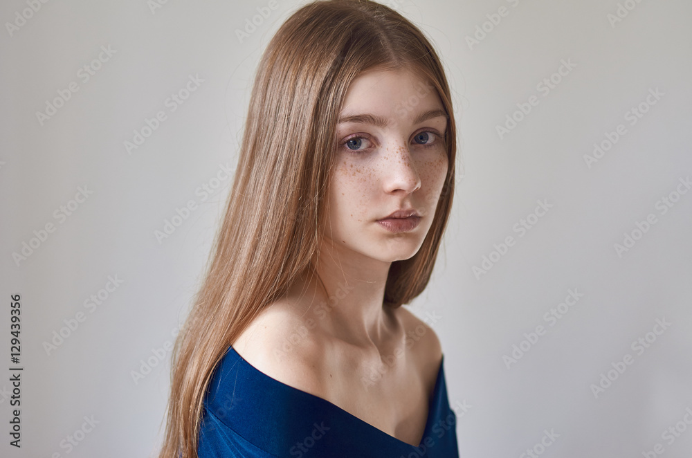 Beauty theme: portrait of a beautiful young girl with freckles on her face and wearing a blue dress on a white background in studio Beauty theme: portrait of a beautiful young girl with freckles on her face and wearing a blue dress on a white background in studio
