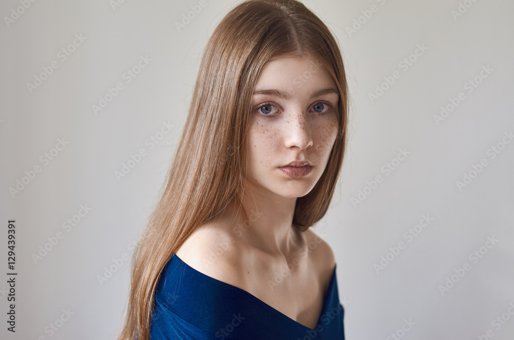 Beauty theme: portrait of a beautiful young girl with freckles on her face and wearing a blue dress on a white background in studio Beauty theme: portrait of a beautiful young girl with freckles on her face and wearing a blue dress on a white background in studio