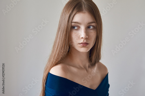 Beauty theme: portrait of a beautiful young girl with freckles on her face and wearing a blue dress on a white background in studio