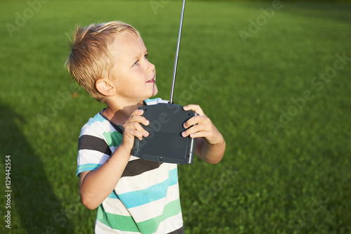 Little child blond boy playing with toy radiocontrolled airplane against green grass lawn background. Holds and operates radio controls

 photo