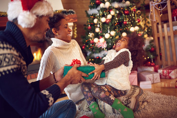 family on Christmas opening gifts sitting on floor at home.