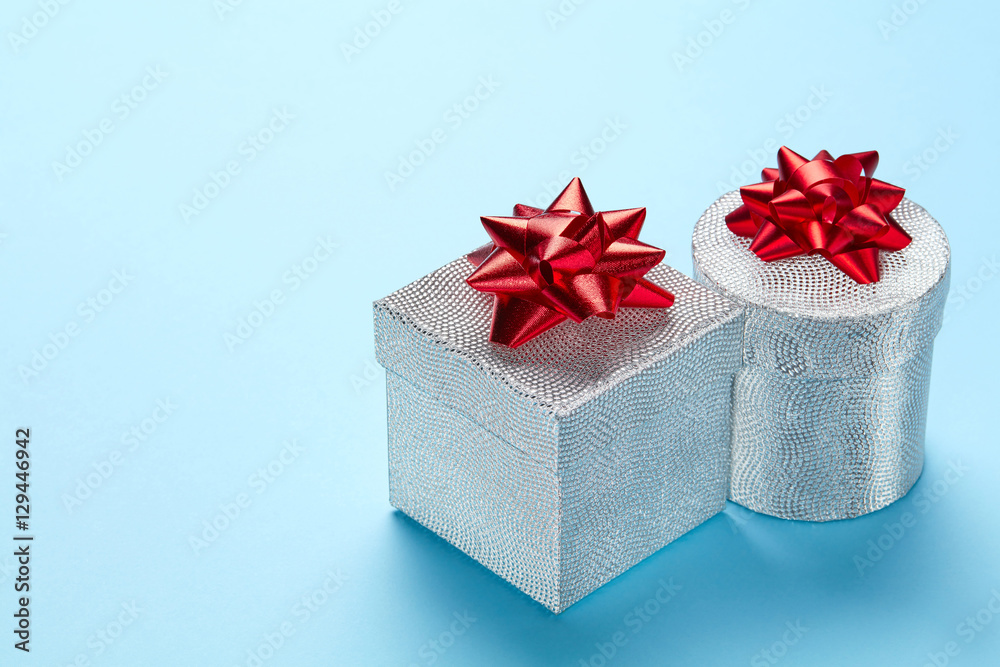 Obraz premium Blue plain background with silver gift and red ribbon