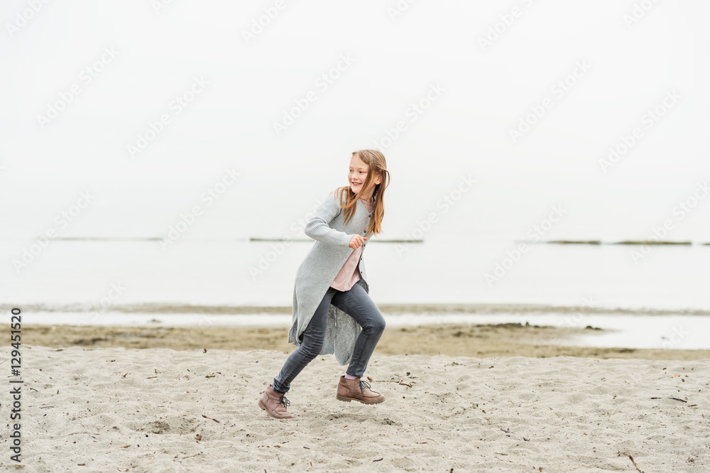 Adorable little girl of 8-9 years old playing by the lake, wearing grey trousers and long cardigan