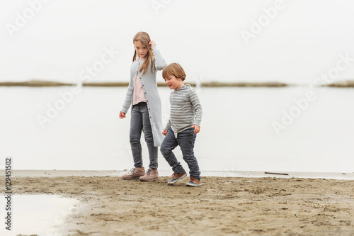 Two little kids playing outdoors by the lake, wearing grey clothes