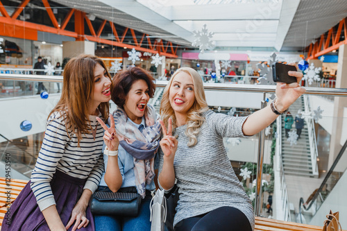 Group of cute girl friends doing some shopping at a mall and taking a selfie with a smartphone
