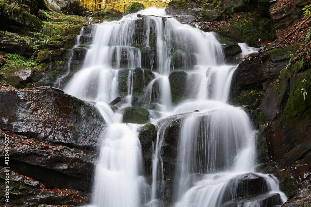 Beautiful view of the waterfall in the beech forest in the golden autumn season.