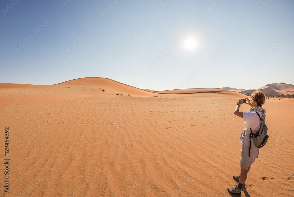 Tourist holding smart phone and taking photo at scenic sand dunes at Sossusvlei, Namib desert, Namib Naukluft National Park, Namibia. Adventure and exploration in Africa.