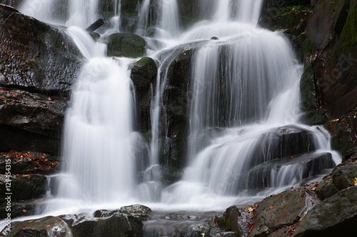 Beautiful view of the waterfall in the beech forest in the golden autumn season.