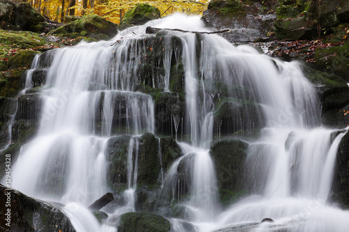 Beautiful view of the waterfall in the beech forest in the golden autumn season.