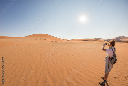 Tourist holding smart phone and taking photo at scenic sand dunes at Sossusvlei  Namib desert  Namib Naukluft National Park  Namibia. Adventure and exploration in Africa.