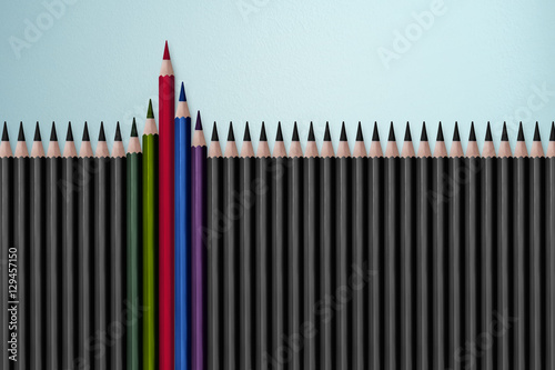 Red pencil standing out from crowd of plenty identical black fellows on white table. Leadership, uniqueness, independence, initiative, strategy, dissent, think different, business success concept