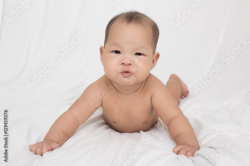smiling surprised baby lying on a white bed. Baby born in Thailand, Asia. Infants aged 5 months