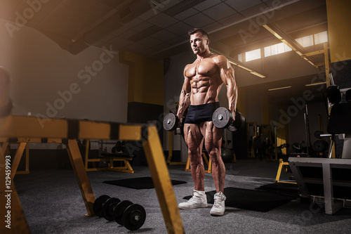 Muscular bodybuilder guy doing exercises with dumbbell