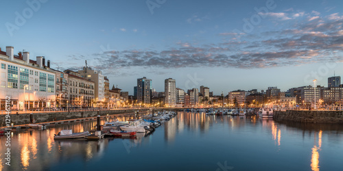 Yatchs and pier in leisure port on maritime fishing district of Gijon, Spain, Europe. Beautiful reflection on calm sea water of boats, buildings, sky at dusk at touristic cultural travel destination.