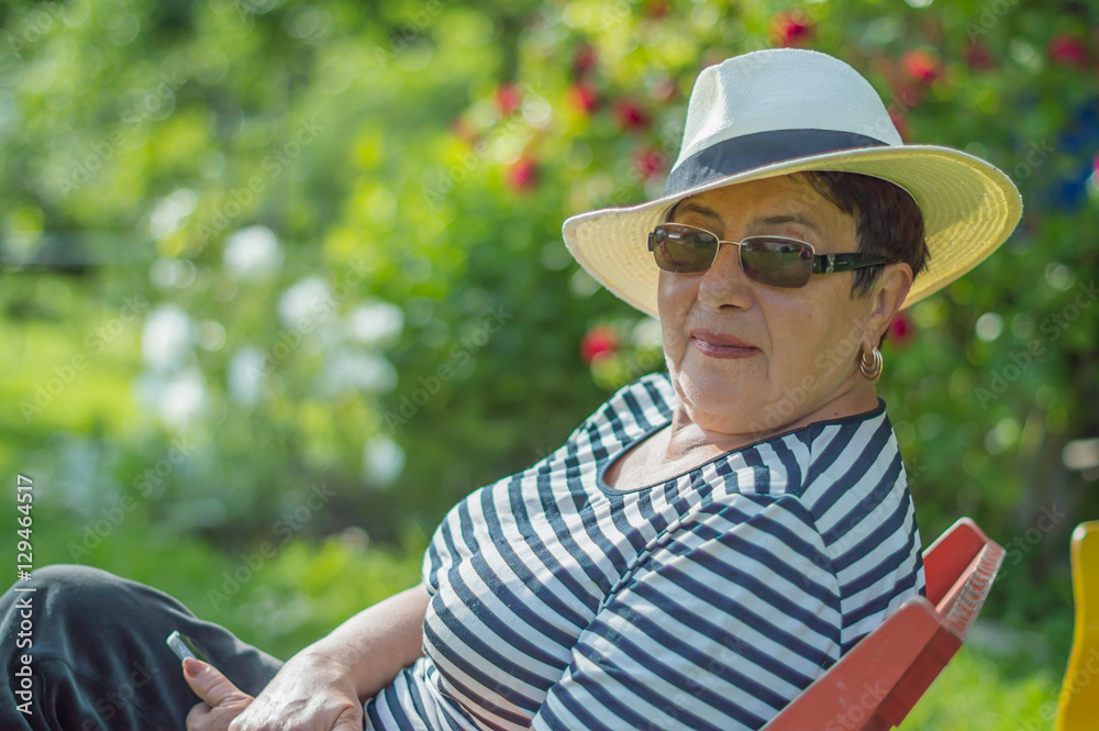 nice elderly lady in a hat and sunglasses sitting on a chair in the garden