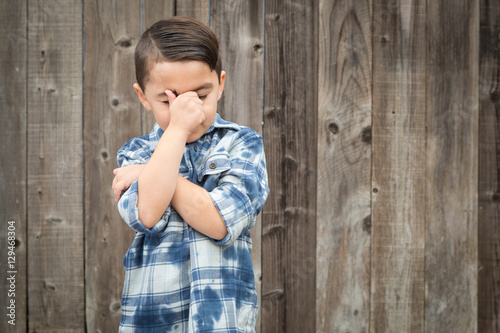 Young Frustrated Mixed Race Boy With Hand on Face Against Wooden Fence. © Andy Dean