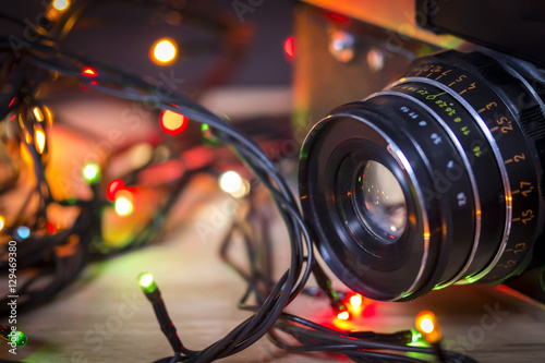 Vintage camera lens with garland christmas lights on colorful bokeh background. Mockup for holiday new year greeting card